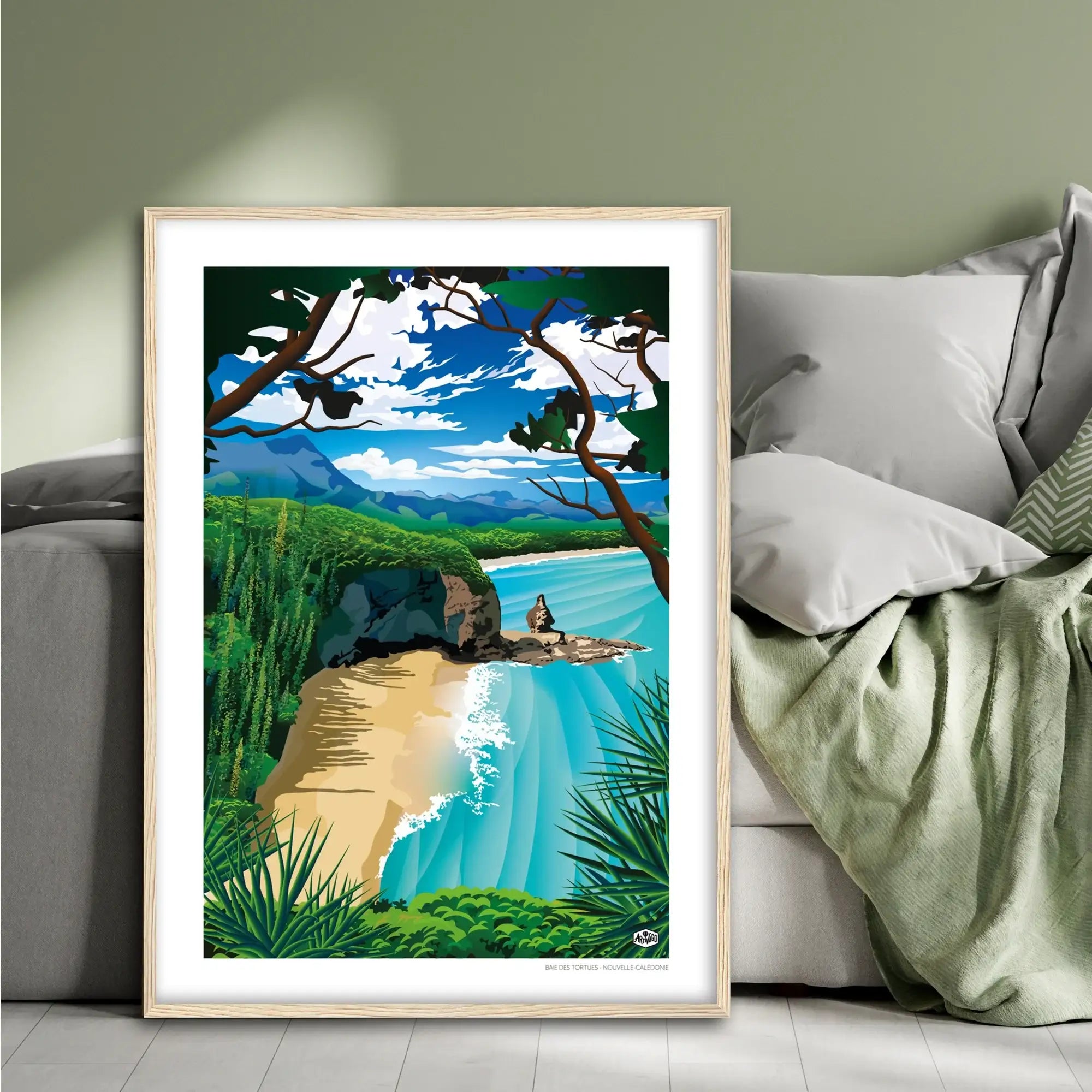 Affiche Nouvelle-Calédonie « Baie des Tortues », format 50×70 cm avec cadre en bois, posée contre un lit dans une chambre à la décoration douce et naturelle