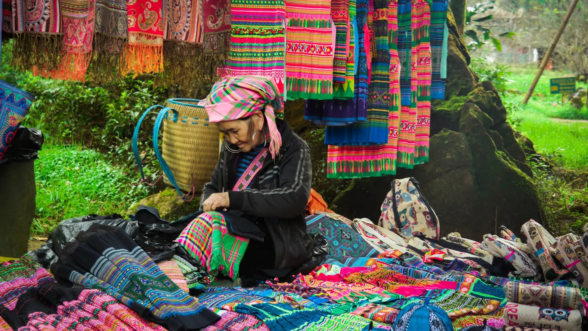 Femme Hmong entourée de textiles brodés et d’objets artisanaux