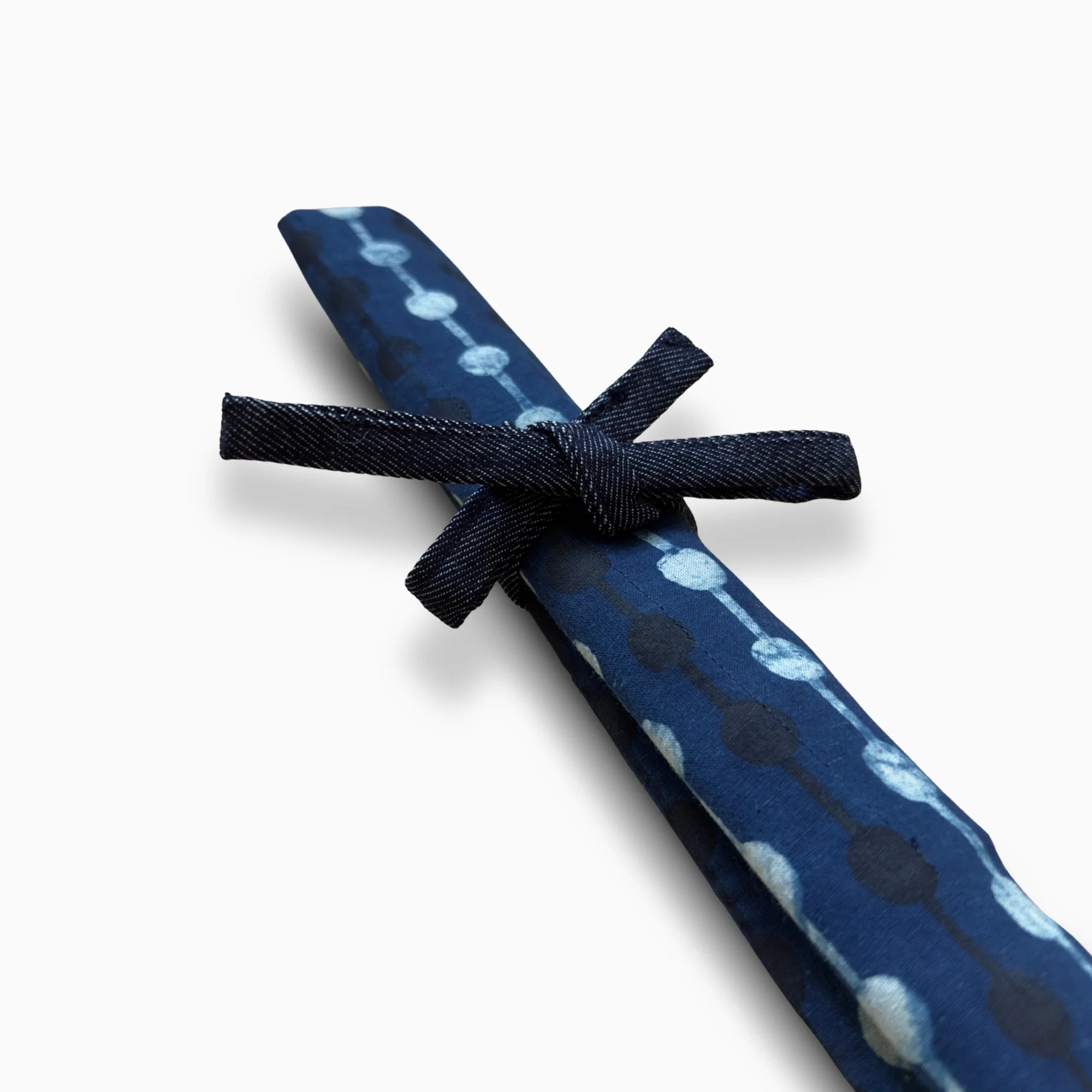 Détail du porte-couverts roulé – tissu batik bleu artisanal – gros plan sur le nœud en jean